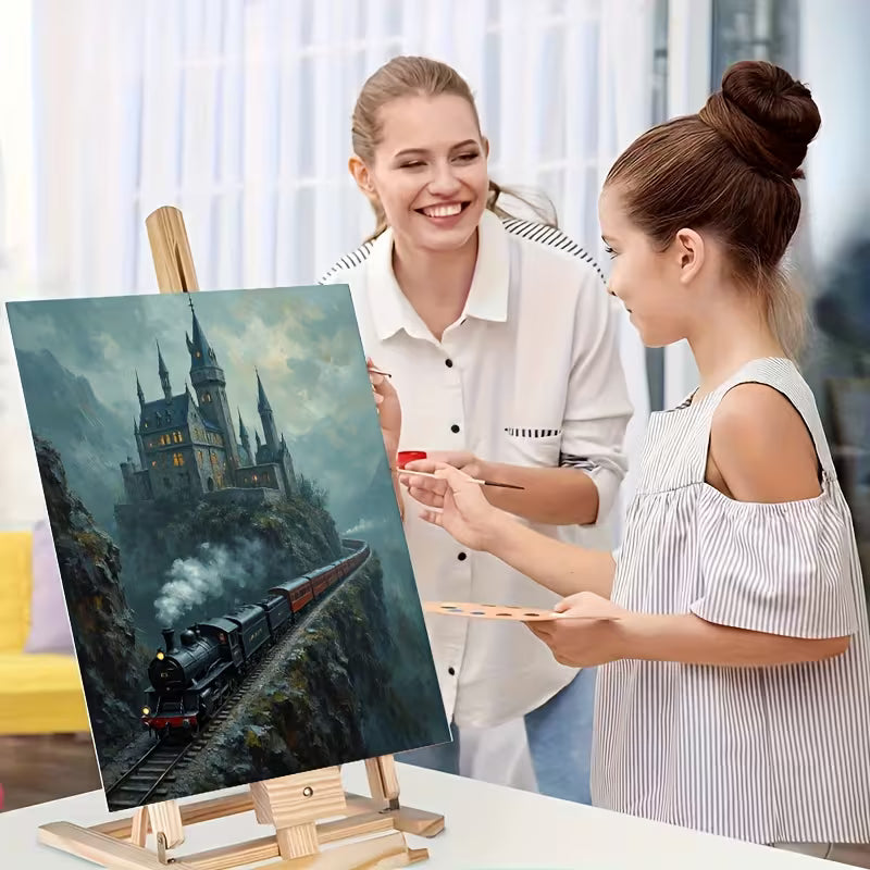 Жена и дете рисуват картина с парен влак и замък върху платно на статив
