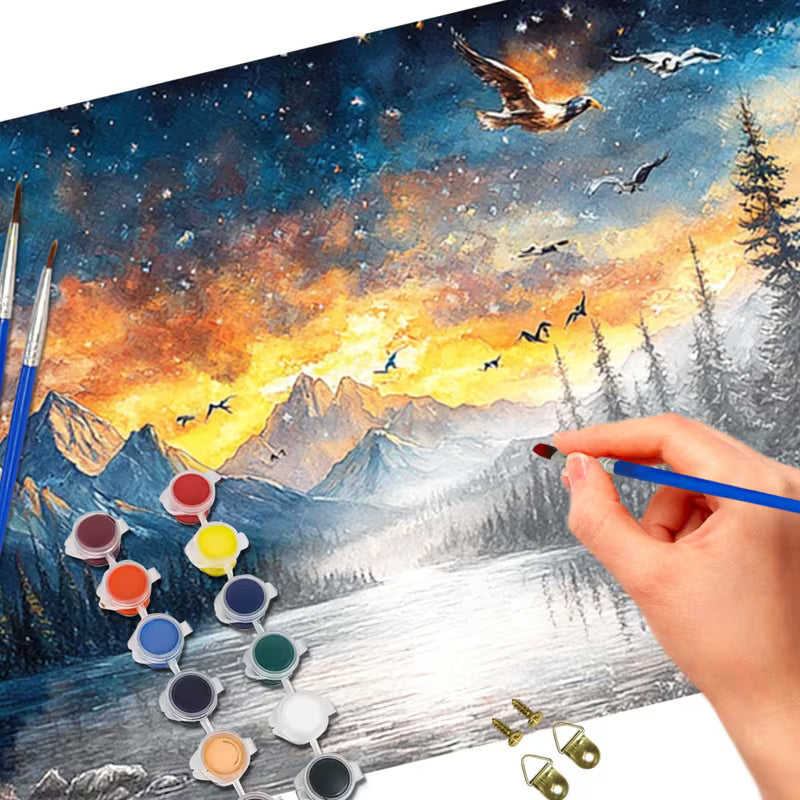 Картина за оцветяване по номера с панорамна сцена на планини, езеро и летящи птици при залез, показан в процес на изработка с четка и цветни мъниста.