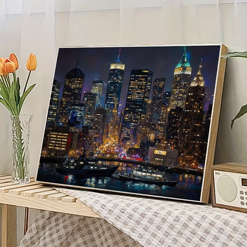 Готова картина по номера с нощен градски пейзаж и небостъргачи, поставена върху маса в уютен интериор
