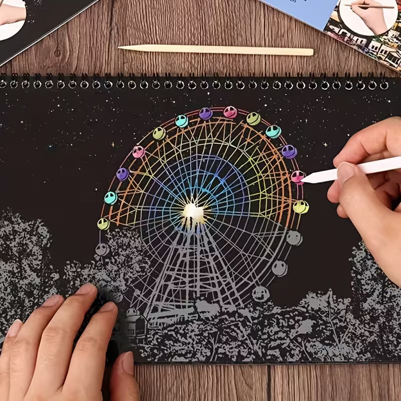 Скреч картина в процес на работа, показваща виенско колело с цветни светлини върху черен фон, докато ръка изтрива покритието със скреч писалка и разкрива ярките детайли на нощната сцена.